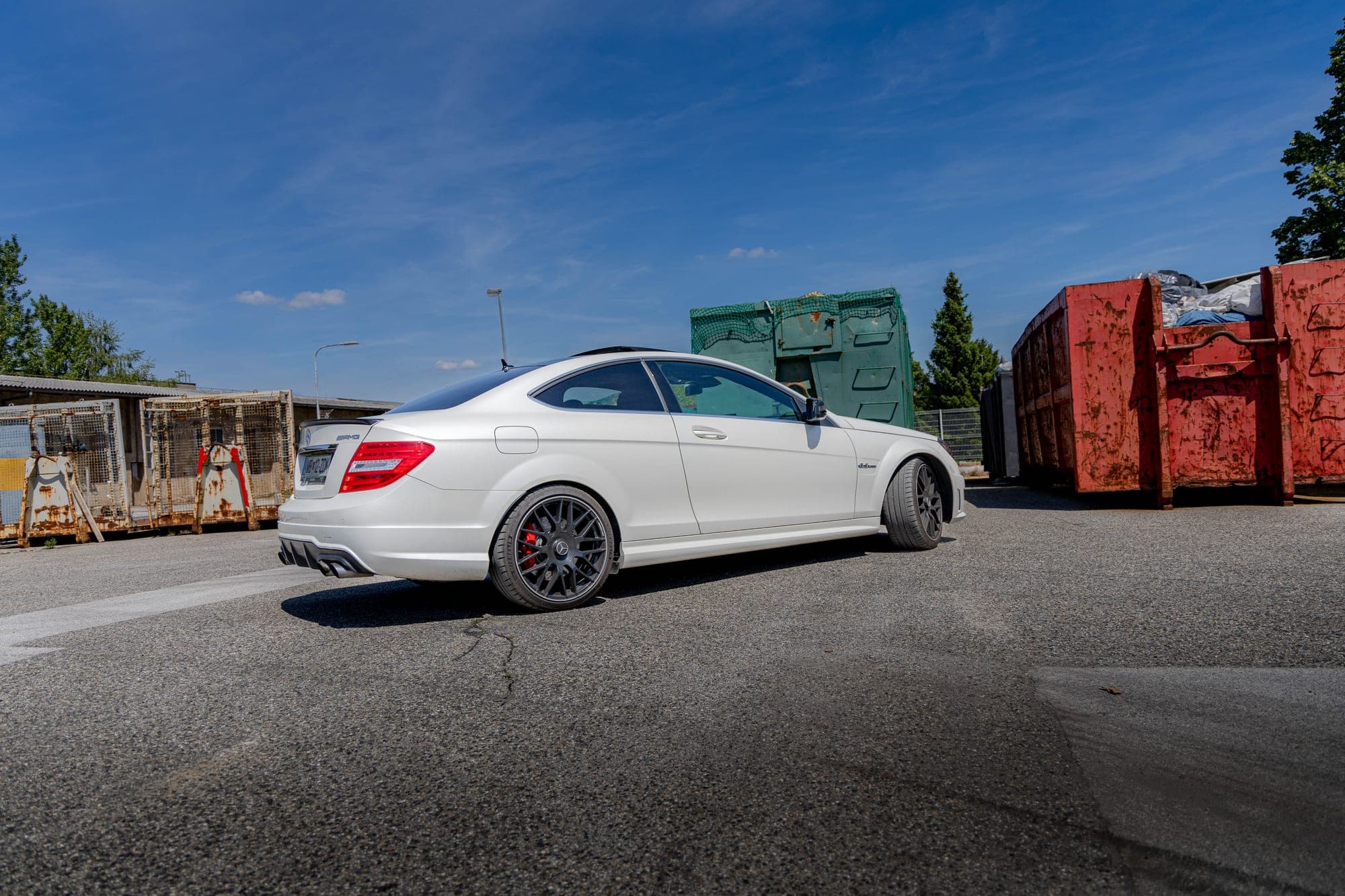 Zadnji del belega AMG coupéja pred kontejnerji